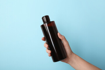 Poster - Woman with shampoo bottle on light blue background, closeup