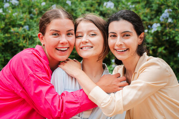 Three young caucasian women hugging outdoors, smiling and enjoying a moment of friendship and togetherness. Girls showcasing happiness, bonding, and positive energy in a casual and relaxed setting.