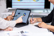 © Wasana - Business team analyzing financial data on tablet and taking notes in meeting