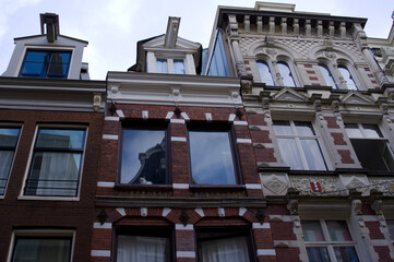 Curioso gato blanco asomado en la ventana de un tradicional edificio holandés con ladrillos y ornamentos una tarde nublada en Ámsterdam