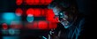 © HadK - A concerned executive in glasses holds a phone, illuminated by red warning lights in the background, suggesting cybersecurity or crisis.