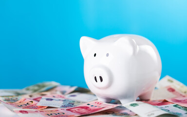 White piggy bank and Chinese Yuan currency placed on a table, set against a light blue background. The image symbolizes savings and financial management with a focus on China's economy