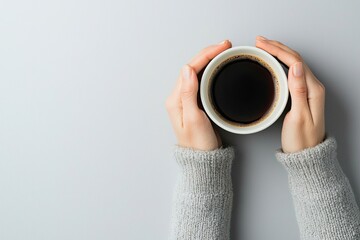 Wall Mural - Woman's hands holding a cup of coffee on a light background, top view. Flat lay with copy space for design