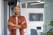 © Liubomir - Confident man smiling in office doorway with arms crossed. Modern style with red shirt and white t-shirt. Represents confidence, professionalism, positivity in professional environment.