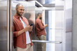 © Liubomir - Man standing in elevator using smartphone, leaning against mirror wall, smiling effortlessly, dressed in casual attire. Scene depicts connectivity, communication, modern technology, daily routine.