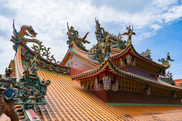 An ornate temple rooftop with intricate dragon sculptures, colorful decorations, and vibrant details under a partly cloudy sky