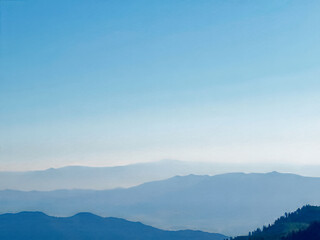 Wall Mural - The sky is blue and the mountains are in the background. The mountains are covered in trees and the sky is clear