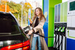 © maxbelchenko - Beautiful woman filling her car with gasoline at the gas station. Online pay. Woman pays for a gas station using an app on her phone.