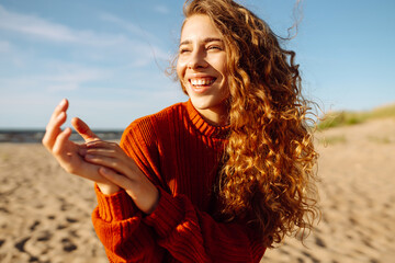 Portrait of a beautiful woman on the beach at sunset at the windy autumn day. Fashion style. Travel, weekend, relax concept.