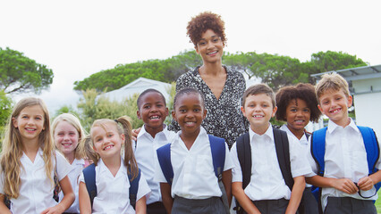 Wall Mural - Outdoor Portrait Of Elementary School Pupils With Teacher Wearing Uniform Standing On Playing Field