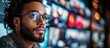 © Alienmarsh - A young man with a beard and glasses looks thoughtfully at a wall of screens displaying various images.