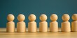 © kiimoshi - A row of wooden figurines representing unity and teamwork on a wooden surface against a simple backdrop.