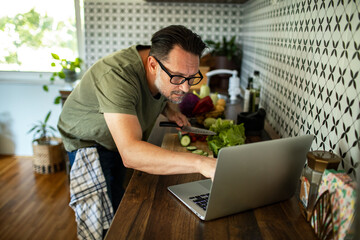 Man following recipe online while preparing vegetables in kitchen