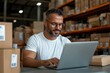 © Milos - This image shows a focused worker in a white shirt and glasses typing on a laptop within a warehouse setting, surrounded by cardboard boxes, under soft lighting.