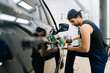 © dikushin - Closeup of mechanic worker in cap polishing door of luxury car in auto repair shop using with orbital polisher. Expert car paint technician using car polisher to polish car with refinement.