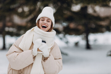 Happy laughing young woman with coffee hot drink cup enjoys winter weather at snowy winter park