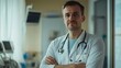 © florynstudio3 - A young doctor with a serious expression stands in a hospital room, looking directly at the camera. He is wearing a white coat and a stethoscope.