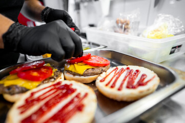 Wall Mural - A person in gloves prepares gourmet burgers, adding fresh toppings and sauce. The focus is on the vibrant ingredients and meticulous cooking process, highlighting the art of burger making