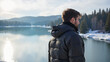 © Andrey - Contemplative man in puffy jacket standing by tranquil lake surrounded by snowy mountains