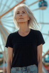 An older woman with gray hair stands confidently in front of a Ferris wheel, gazing upward. The sun shines brightly, highlighting her serene expression and casual attire while capturing the joyful atm