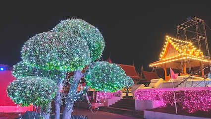 Decorative colorful illuminated lighting on tree and traditional Thai style houses in the temple at night at Thailand