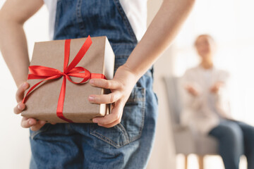 Wall Mural - Focused shot of little small girl daughter giving present gift box making surprise to her mother on Birthday Christmas Mother`s day, hiding present behind at home