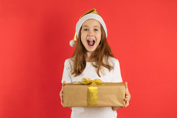 Funny teenage girl in santa hat happily holding a gift on red background, copy space.