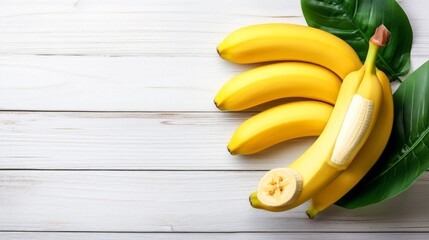 Wall Mural - Four yellow bananas, one sliced in half, with green leaves on a white wood background.