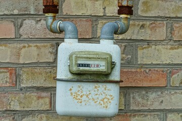 one home iron square painted industrial meter with white display and numbers dirty old gas meter with two pipes on yellow brick wall outdoors