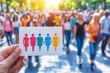 © Leo - Colorful hand drawn symbols of men and women on a white card held up against a blurred crowd in the background symbolizing gender diversity equality and representation in society