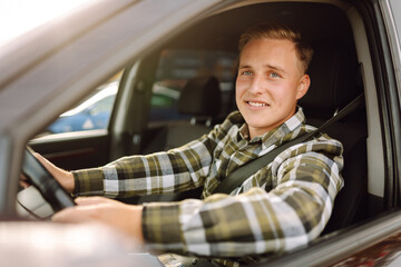 Young man in a car smiling and looking at the camera. Buying and renting a car. Car travel, lifestyle concept.