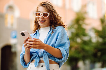 Young woman walking around old street and using smartphone. Online Communication with friends. Technology, connection, blogging, modern lifestyle concept.