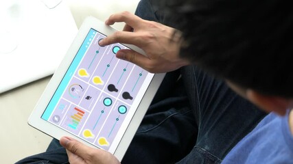 A person is holding a smartphone that is displaying a home automation app. The app has a light, camera, and security icon. The person is likely using the app to control their home's lighting, security