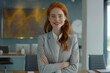 © Isuru - Young redhead businesswoman smiling at camera in office.