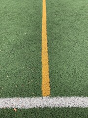 A centered view of a sports field showcasing two parallel lines: a vibrant yellow line running vertically and a bright white line running horizontally across green artificial turf.