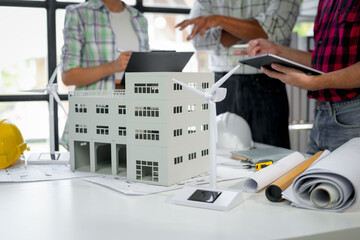 Wall Mural - architects team working on project of ecological modern building with wind turbine using model and l