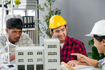 Wall Mural - architects wearing hard hats smiling and working together on a building model in the office