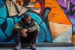 © tynza - A homeless man sitting against a graffiti-covered wall, with a distant and hopeless expression on his face.