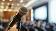 © stockagency - A microphone in focus with an audience blurred in the background, suggesting a speaking event.