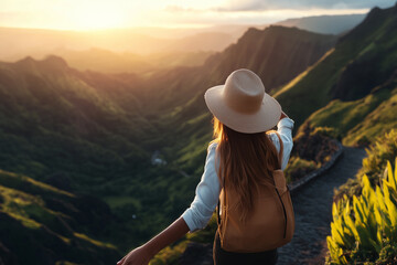 A woman stands on a scenic mountain trail, facing a breathtaking sunset over lush green valleys. She wears a wide-brimmed hat and a backpack, with her arms outstretched as if embracing the view. 