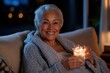 © Milos - A joyful older woman in comfortable indoor attire holds a lighted glass against a backdrop of warm, ambient room lighting, exuding warmth and happiness.