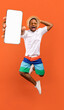 © Prostock-studio - Cool mobile offer. Excited jumping black guy demonstrating smartphone with white screen on orange studio background, collage with mockup copy space for app or website design