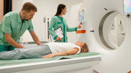 Wall Mural - A patient is positioned on an MRI scanner table, while two healthcare professionals in green uniforms operate the machine and monitor the process, creating a modern and efficient medical environment.