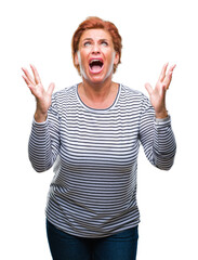 Wall Mural - Atrractive senior caucasian redhead woman over isolated background crazy and mad shouting and yelling with aggressive expression and arms raised. Frustration concept.