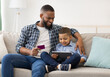 © Prostock-studio - Online Shopping. Black Father And Son Using Digital Tablet Buying Things And Making Payment Via Credit Card Sitting On Couch At Home. Modern Family Shopping Concept