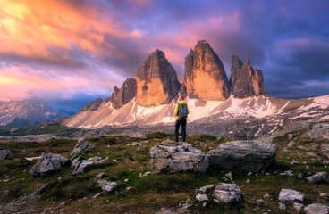 Wall Mural - girl with backpack on the stone and high mountain peaks at colorful sunset in autumn. tre cime, dolo