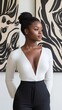 © Raul - A young Black woman with her hair in a bun,  looks to the right.  She is wearing a white long-sleeved top and black pants, standing in front of art.