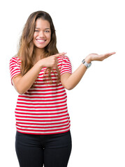 Wall Mural - Young beautiful brunette woman wearing stripes t-shirt over isolated background amazed and smiling to the camera while presenting with hand and pointing with finger.