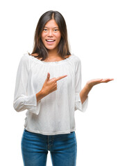 Wall Mural - Young asian woman over isolated background amazed and smiling to the camera while presenting with hand and pointing with finger.