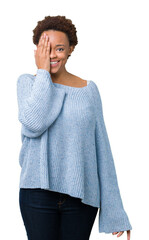 Wall Mural - Young beautiful african american woman wearing a sweater over isolated background covering one eye with hand with confident smile on face and surprise emotion.